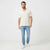 A man wearing a textured cream short-sleeve polo shirt, light blue jeans, and white sneakers, standing against a plain white studio background.
