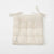 A square, quilted cotton muslin seat pad in a natural cream color, featuring tie straps at the top corners and a small sewn-in label on the lower left, shown against a plain white background.