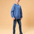 A child model wearing an oversized blue hoodie and dark blue jeans, standing against a solid warm beige background.