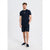 A man modeling a navy blue short-sleeve crewneck t-shirt with a small embroidered logo on the left chest, paired with matching navy shorts and dark slip-on shoes, against a light gray studio background.
