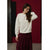 A woman wearing a cream-colored crewneck sweatshirt with tonal circular embroidery and a dark burgundy pleated maxi skirt, standing against a dark red wall.