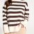 A person wearing a knit sweater with horizontal dark brown and cream stripes, paired with light beige pants, against a plain light background.