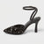A single black pointed-toe high heel with an ankle strap, covered in black sequins and adorned with small white pearl-like embellishments, shown against a light gray background.