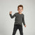 A young boy modeling a dark gray long-sleeve crewneck sweatshirt with a tonal chest graphic, paired with black jeans and black sneakers, against a light gray studio background.