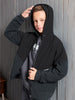 Young person wearing a black hoodie with a zipper, standing against a wooden panel background.
