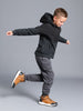 Child wearing a black hoodie and gray pants with brown shoes on a gray background