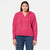A woman modeling a bright pink ribbed knit pullover hoodie with drawstrings and a V-neck, paired with blue jeans, against a plain white background.