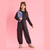 A young girl modeling a dark gray two-piece lounge set consisting of a long-sleeve crop top and matching cargo pants, holding a purple notebook against a solid pink background.