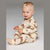 A baby sitting on a light gray studio background wearing a cream-colored footed pajama top and pants set with a brown and black reindeer print and small red accents.