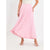 A model wearing a light pink pleated maxi skirt with a layered ruffle hem, paired with a cream top and clear strap sandals, set against a plain white studio background.