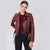 A woman modeling a dark burgundy faux leather moto jacket over a matching burgundy top and black pants, shot against a solid light gray background.