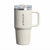 A Stanley travel mug in off-white with a matching handle, a clear lid, and a silver metal band near the top. The Stanley logo is printed vertically on the front.
