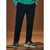 A person wearing dark navy drawstring trousers with a green sweatshirt and chunky sneakers, standing on a wooden platform against a warm brown studio background.