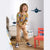 A young child stands in a child's bedroom wearing a brown long-sleeve pajama top with a colorful cartoon dinosaur print and tan pants.