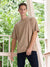 Man wearing a beige t-shirt and dark pants standing on a balcony with greenery in the background