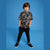 A young boy modeling a short-sleeve t-shirt with a black and gray Mickey Mouse pattern, paired with black pants and black sneakers, standing against a solid blue studio background.