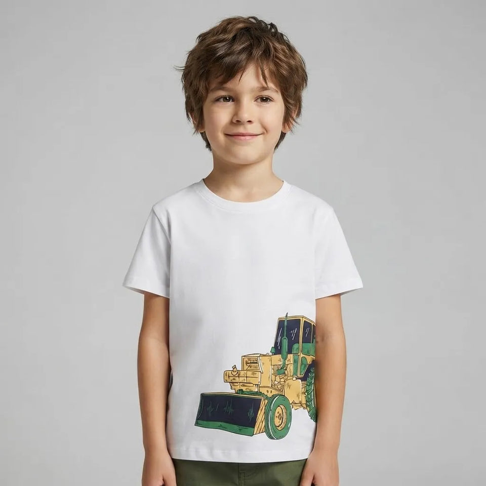 A young boy with brown hair wearing a white crewneck t-shirt with a graphic of a yellow and green bulldozer, standing against a solid gray studio background.