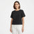 A woman modeling a black short-sleeve top with eyelet cutout detailing on the sleeves, paired with white pants, against a plain white studio background.