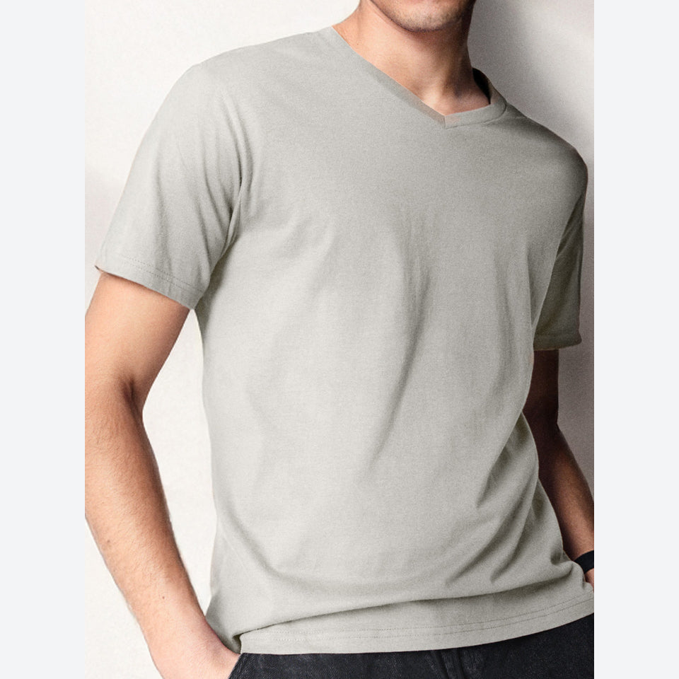 A man wearing a light gray v-neck t-shirt, cropped from the chin down, against a plain off-white background.