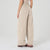 A person shown from the back wearing high-waisted, wide-leg pants in a light beige or oatmeal color, paired with brown shoes, against a plain light gray studio background.