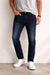 Person wearing dark blue jeans and white sneakers against a plain background