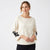 A woman modeling a cream-colored long-sleeve knit top with black floral embroidery on the cuffs, paired with black pants, against a plain white studio background.
