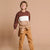 A young boy smiling and posing in a color-blocked sweatshirt with a matching belt and tan pants, set against a solid beige studio background.