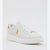 A white leather low-top sneaker with white laces, a thick white platform sole, and gold-tone hardware accents, including a gold horse-and-carriage logo on the side and a gold accent on the toe box. The heel tab is a light tan/beige color.