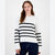 A woman modeling a white knit sweater with horizontal black stripes across the chest and sleeves, paired with dark blue jeans, against a plain white studio background.