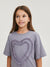 Young girl wearing a gray t-shirt with a heart design on a plain background