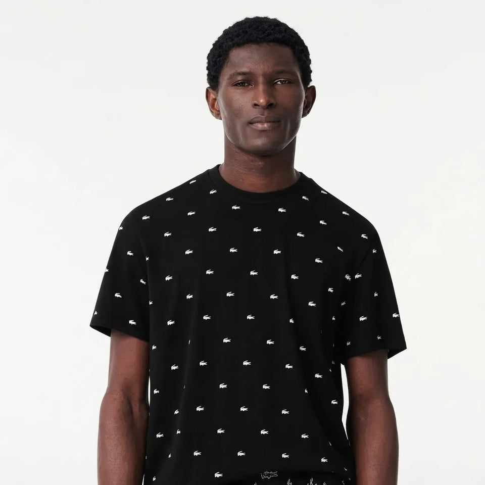 A man wearing a black short-sleeve t-shirt with a small white crocodile pattern, photographed against a plain white studio background.