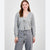 A woman modeling a light gray ribbed knit cardigan with a tie-front detail, paired with gray jeans, against a plain light gray studio background.