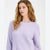 A woman with wavy light brown hair wearing a fuzzy, textured lavender knit sweater, photographed against a clean white studio background.