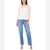 A woman modeling a white lace long-sleeve top with a scalloped hem, paired with light-wash blue jeans and nude heels, against a plain white background.