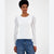 A woman modeling a white ribbed long-sleeve top with sheer polka-dot puff sleeves, paired with blue jeans, against a plain light gray studio background.