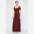 A woman modeling a floor-length burgundy off-the-shoulder gown with a draped, textured fabric and side tie detail, photographed against a light gray studio background.