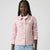 A woman modeling a light pink denim jacket, shown from the waist up against a plain light gray studio background.