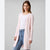 A woman modeling a light pink ribbed knit cardigan over a white top and blue jeans, photographed against a plain light gray studio background.
