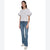 A woman modeling a white short-sleeve top with voluminous ruffled puff sleeves, paired with blue jeans and white sneakers, against a plain white background.