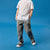 A child model wearing a white crewneck t-shirt, gray cargo pants, and black sneakers, standing against a solid blue studio background.