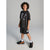 A child model wearing a black graphic t-shirt, matching black athletic shorts, white socks, and black sneakers with orange accents, standing against a neutral gray studio background.