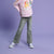 Young girl wearing a pink sweatshirt with cartoon characters and text, standing against a purple background
