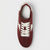 A single low-top sneaker shown from a top-down view, featuring a deep burgundy suede upper, white laces, and white side stripes on a light gray background.