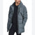 A man wearing a gray hooded puffer jacket with black zippers and trim, layered over a black shirt and dark pants, photographed against a plain white studio background.