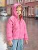 Child wearing a pink quilted jacket on a city street.
