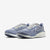 A pair of Nike running shoes in a dusty periwinkle blue and white colorway, featuring a textured knit upper, white Swoosh logo, and white midsole, set against a clean light gray background.