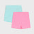 Two pairs of children's shorts in a flat-lay arrangement on a light gray background. The top pair is light aqua blue with small pink polka dots, and the bottom pair is solid bright pink.