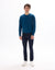 Man wearing a blue sweater and dark jeans on a white background