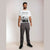 A man modeling a white graphic t-shirt and dark gray outdoor pants against a plain beige studio background.