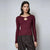 A woman modeling a ribbed long-sleeve knit top in deep burgundy with a circular keyhole cutout at the neckline, paired with dark brown pants, against a light gray studio background.